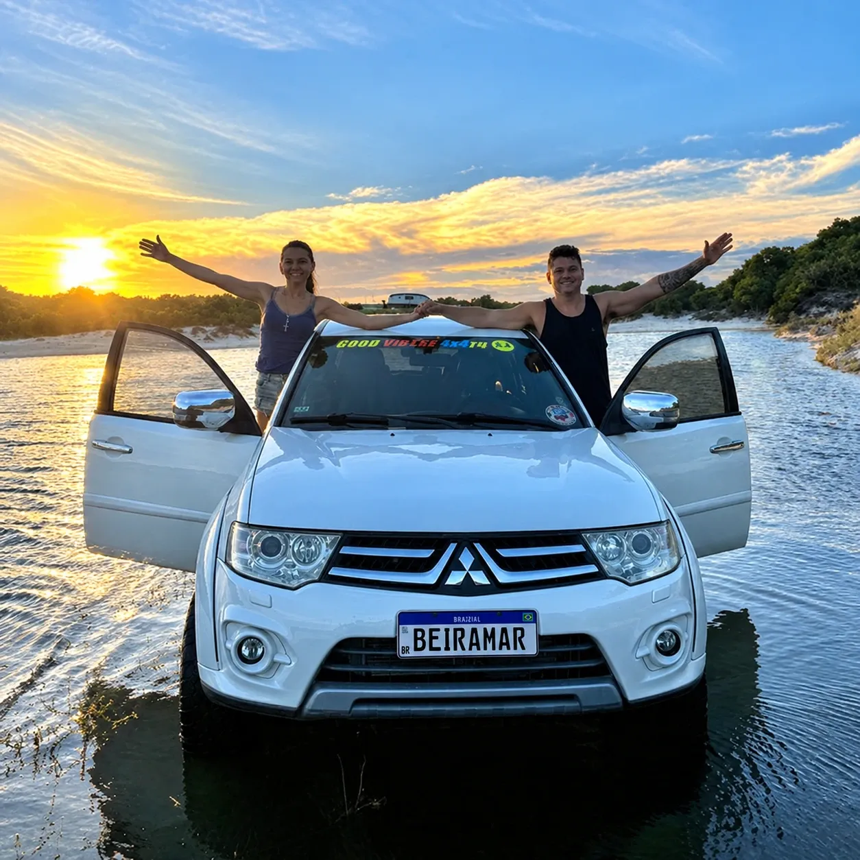 A equipe da Beiramar de braços abertos sobre o 4x4 branco, parado na lagoa ao pôr do sol